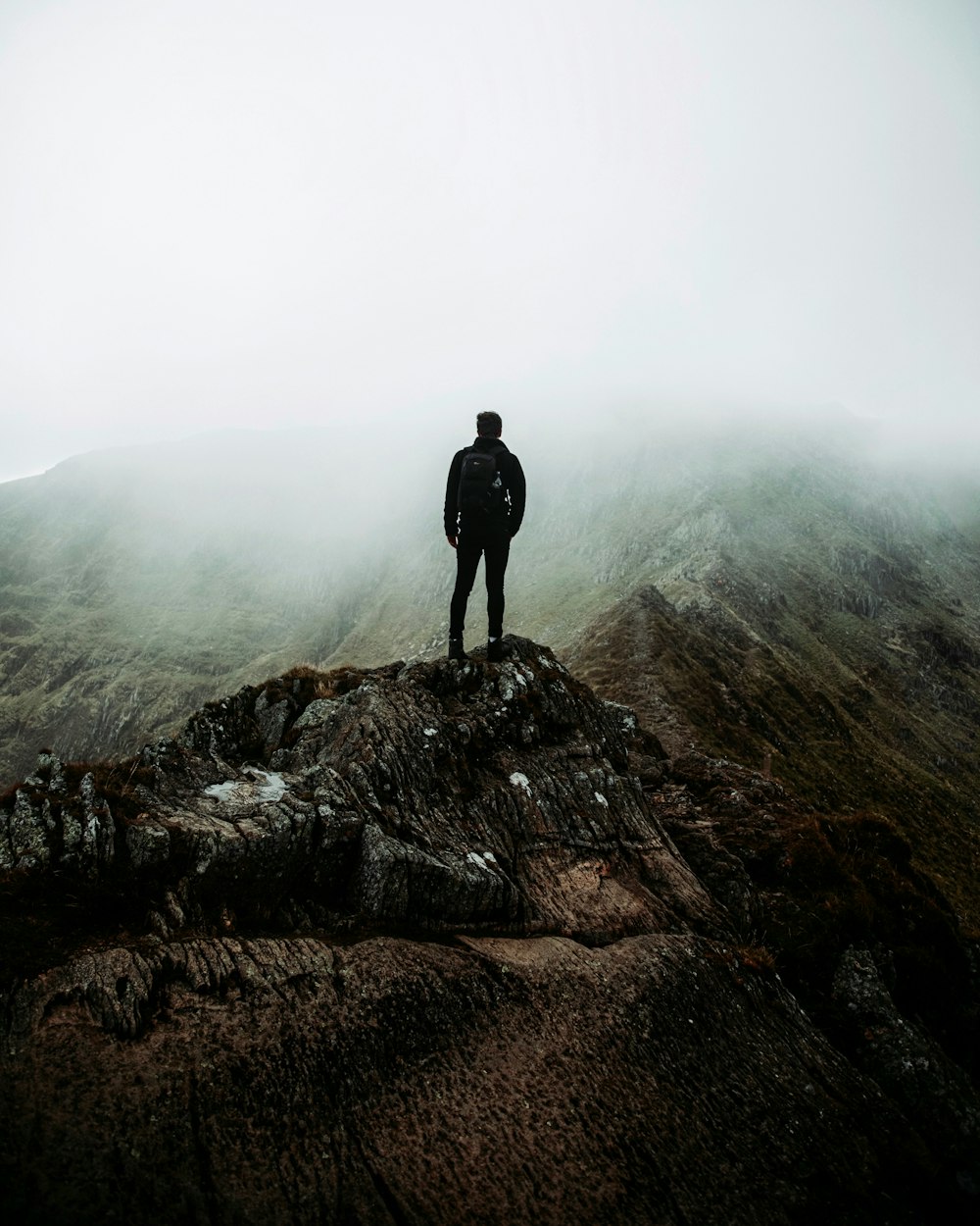 man in black jacket standing on brown rock formation during foggy weather