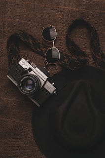 Close-up of a vibrant red beret with a subtle sheen, placed on a marble surface alongside a camera and sunglasses