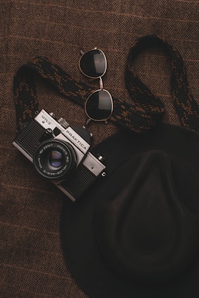 Close-up of a vibrant red beret with a subtle sheen, placed on a marble surface alongside a camera and sunglasses