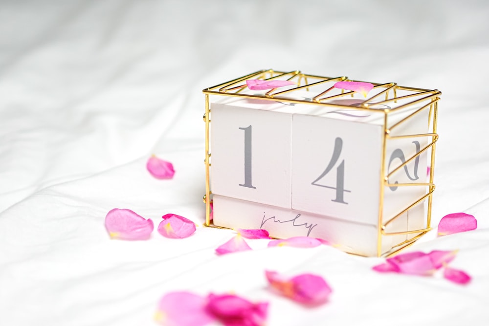 white and gold box with pink petals on white textile