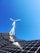 A clear blue sky provides the backdrop for a modern renewable energy setup featuring a wind turbine and solar panels. The sleek, geometric arrangement of solar panels reflects light while the blades of the wind turbine cut through the sky above.
