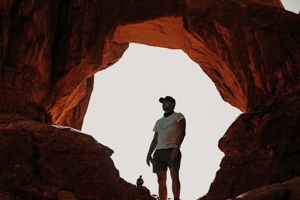 man in gray shirt and black pants standing on brown rock formation during daytime