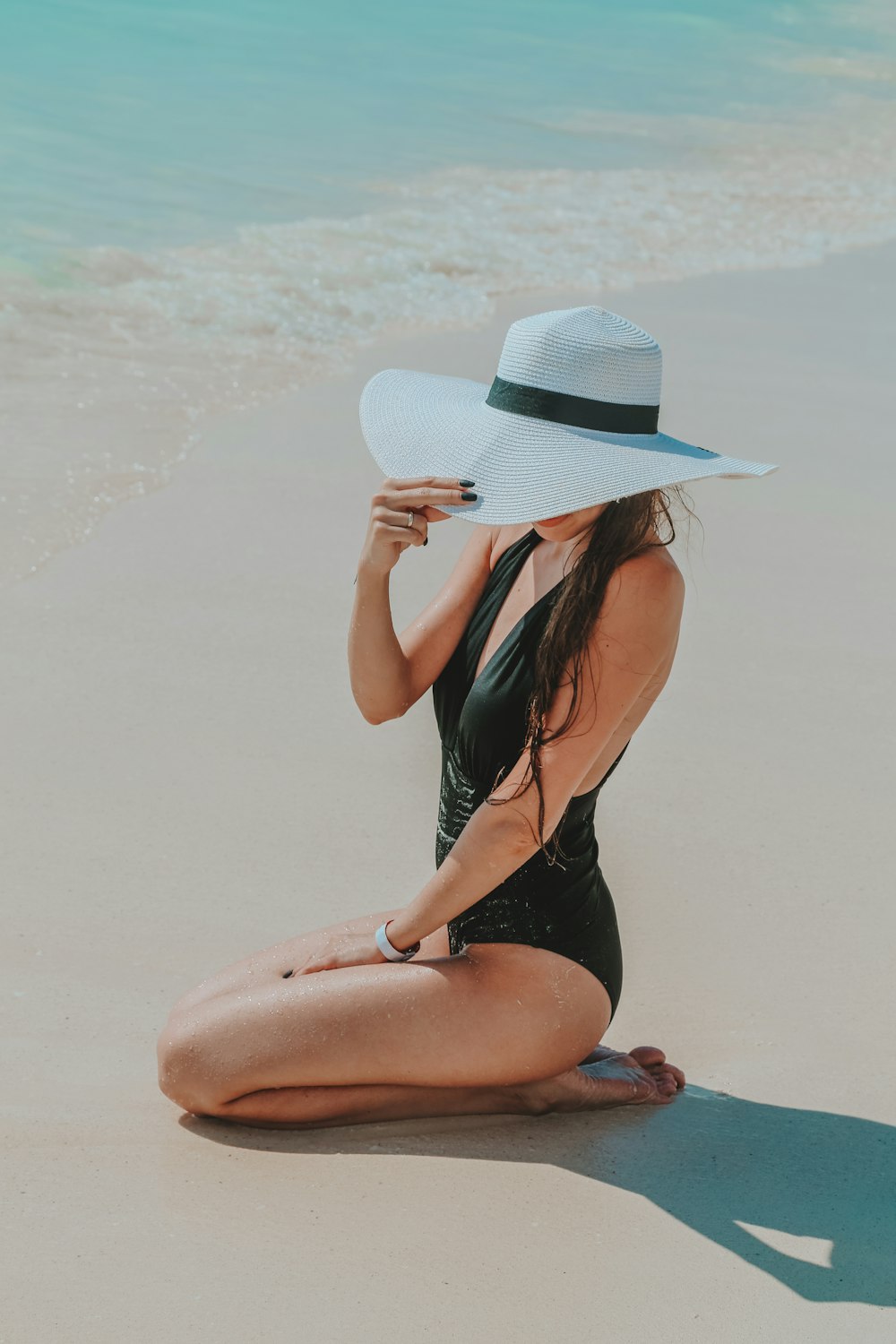 a woman sitting on the beach wearing a hat