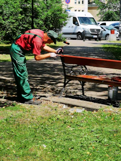 man in red t-shirt and green pants standing near brown wooden bench during daytime