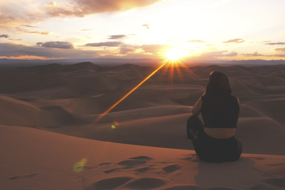 Frau in schwarzer Jacke sitzt bei Sonnenuntergang auf Sand