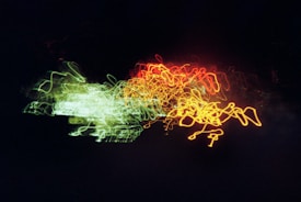 A dynamic array of squiggly neon lights in red, yellow, and green against a dark background, creating an abstract, energetic visual.