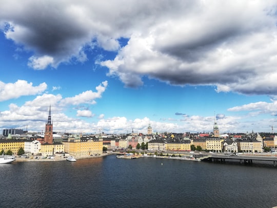 white and brown concrete building near body of water under blue and white cloudy sky during in Mariaberget Sweden