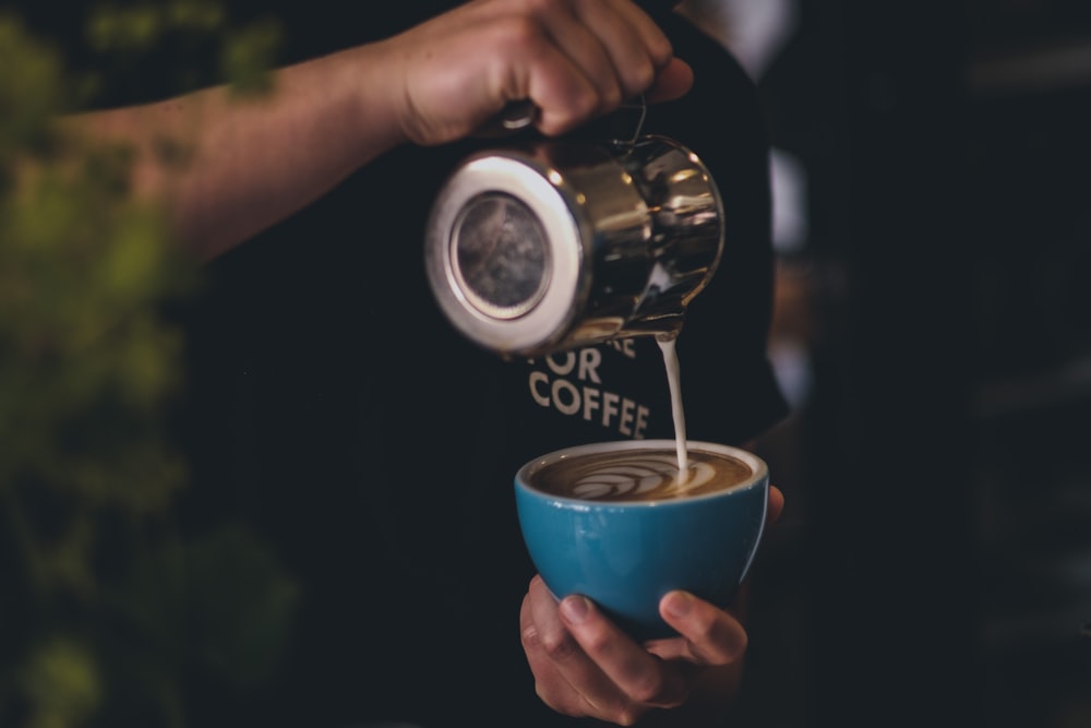 person pouring coffee on blue ceramic mug