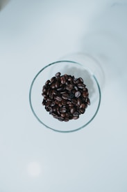 A clear glass container filled with dark roasted coffee beans sits against a clean, white surface creating a minimalistic aesthetic.