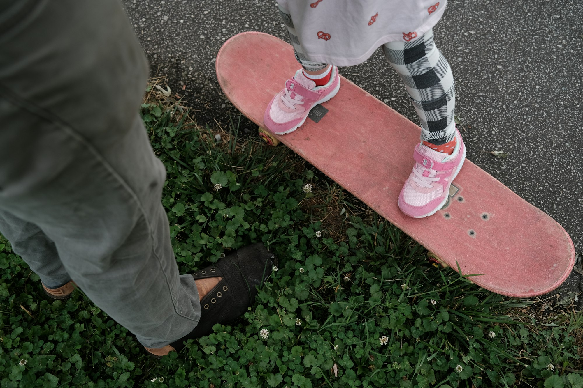 A Dad and his daughter playing together on a skateboard.