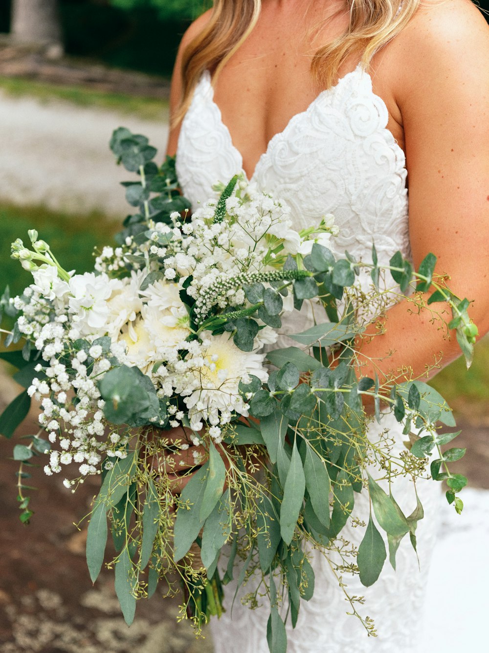 mulher no vestido de noiva floral branco que segura as flores brancas