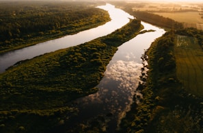 A sweeping aerial view of a winding river cutting through lush, green landscape at golden hour.