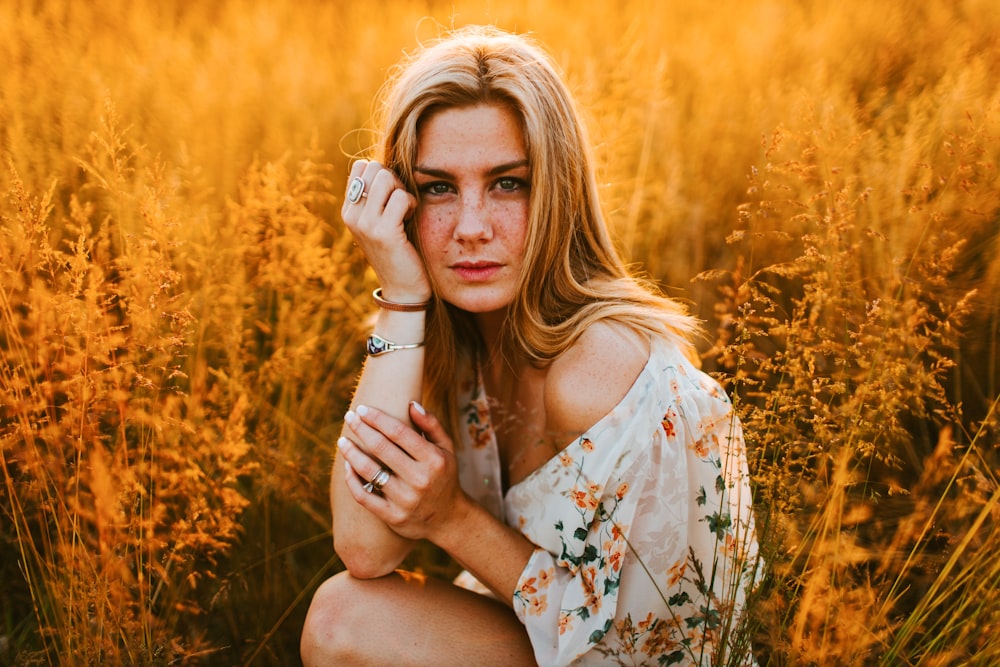 donna in abito floreale bianco e marrone che si siede sul campo di erba marrone durante il giorno