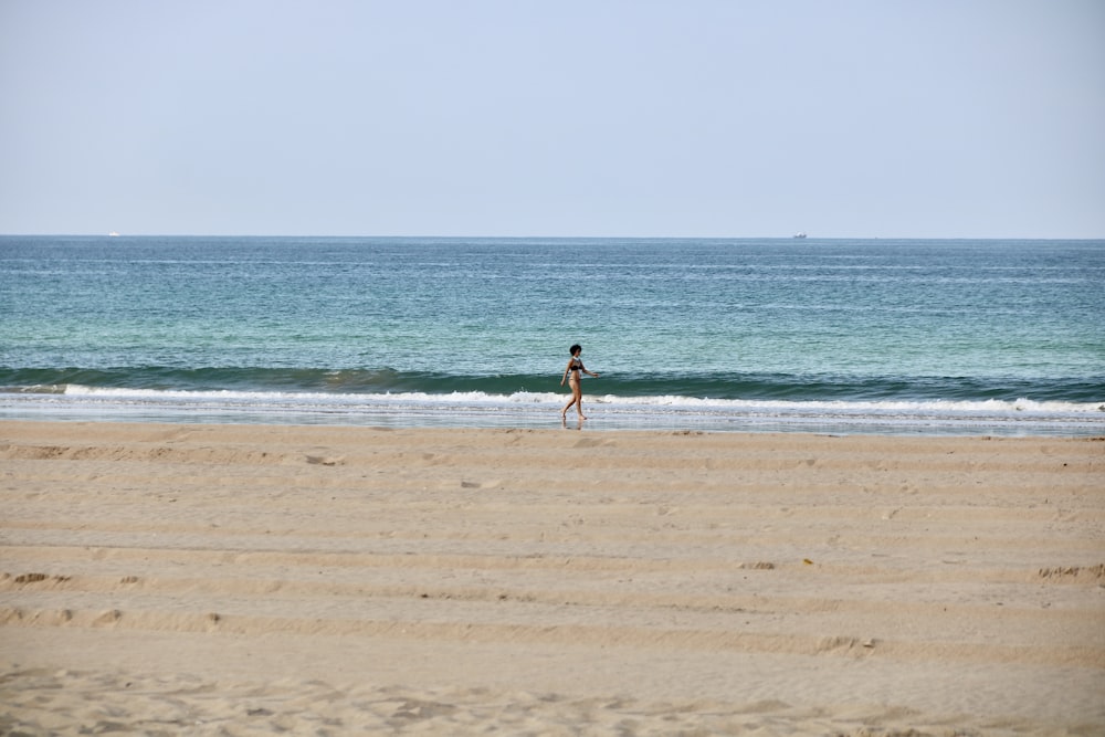 woman in black bikini walking on beach during daytime