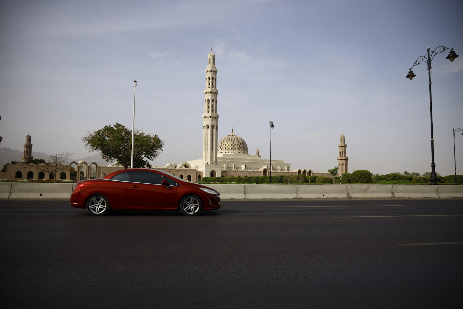 A red car on a broad Muscat road near the Grand Mosque