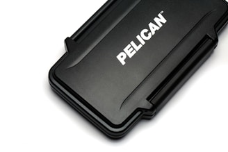 A rectangular black hard case with rounded edges and a textured surface. The case displays the brand name 'PELICAN' in bold white letters across its center.