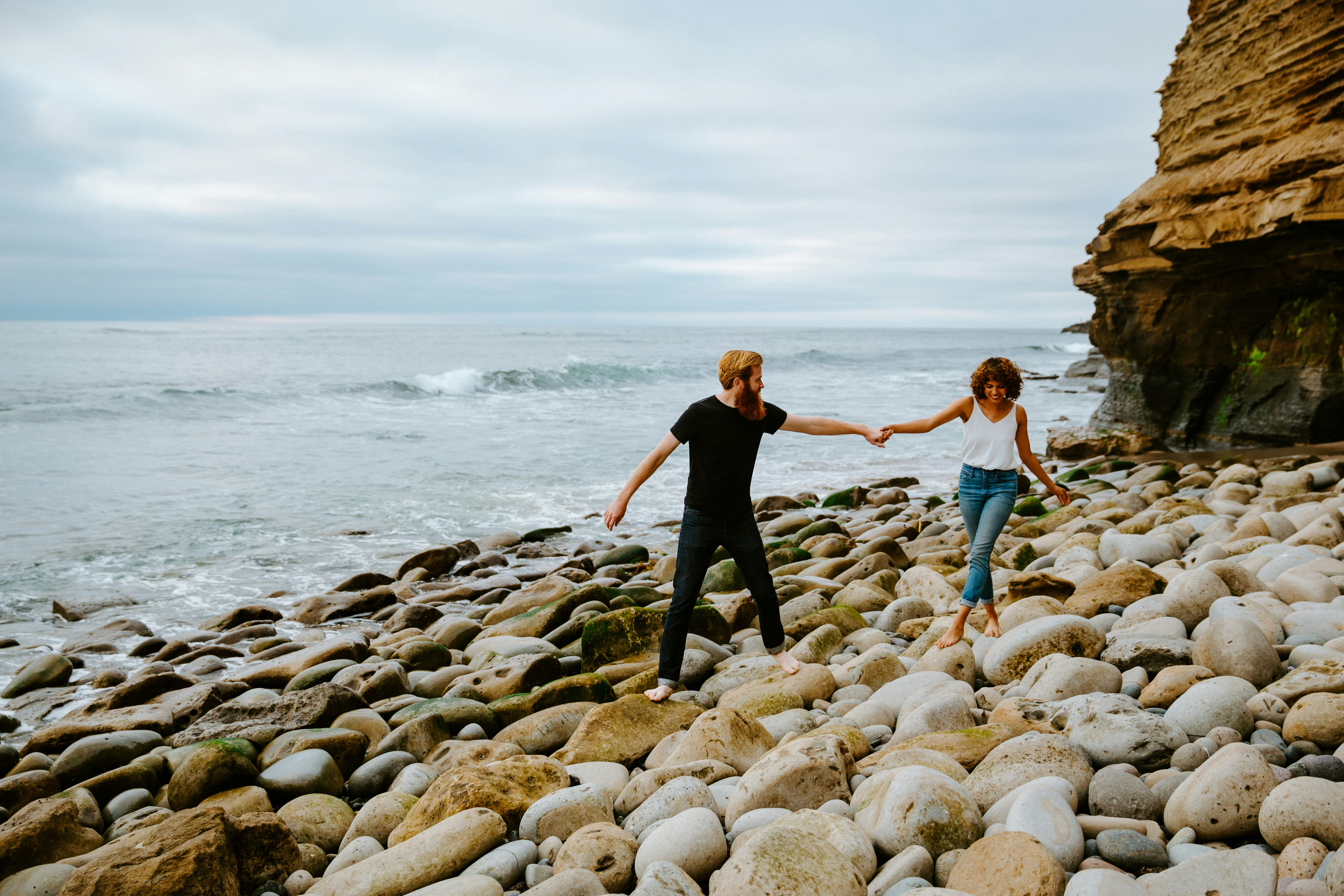 2 women in black tank top and blue denim jeans standing on rocky shore during daytime