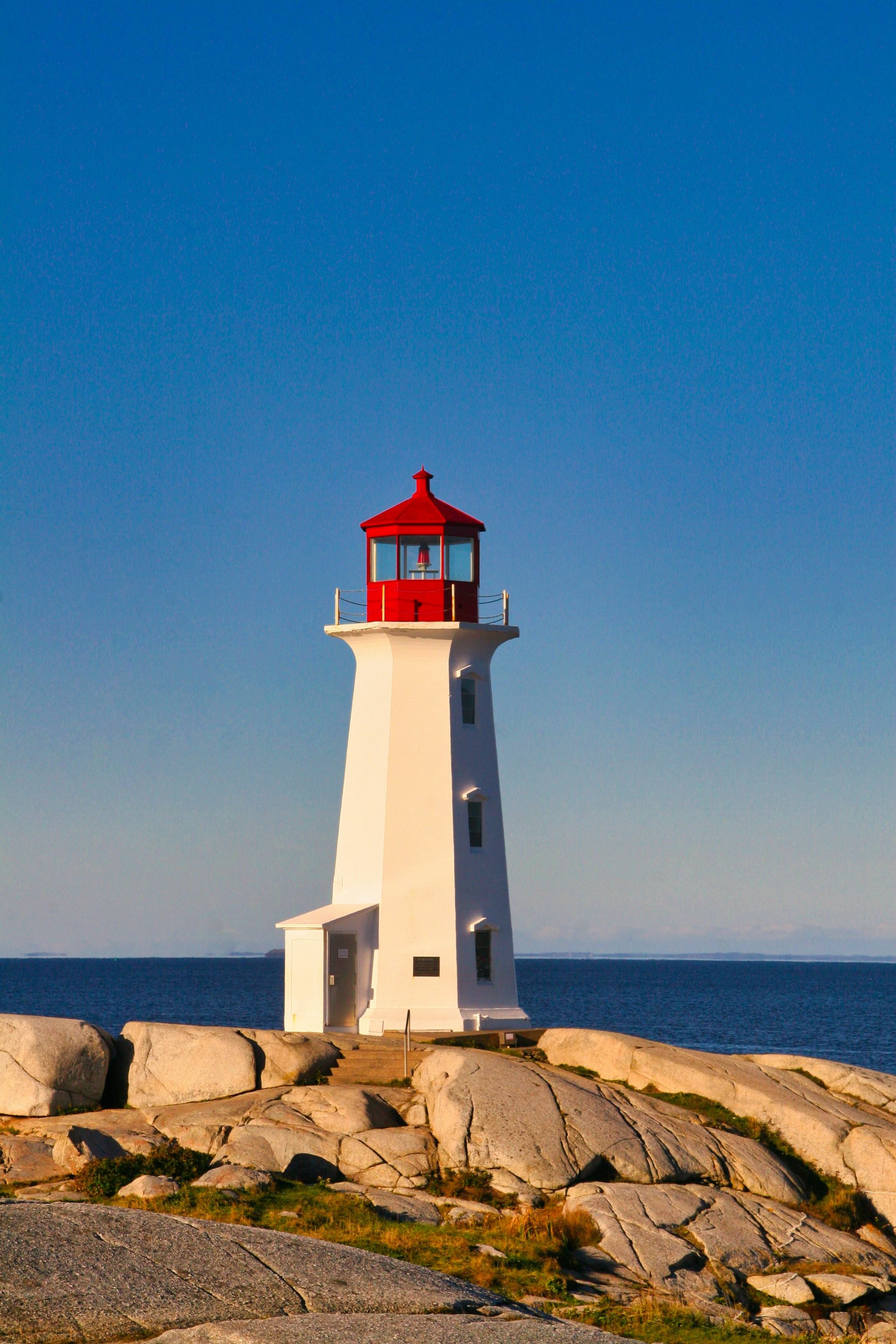 Weißer und roter Leuchtturm in der Nähe des Gewässers tagsüber