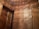 A view of tall, wooden cabinets filling the walls of a room. The cabinets have ornate borders on the doors and brass handles. The wood has a warm, rich color with light reflections creating a shimmering effect. Part of the doorway is also visible.