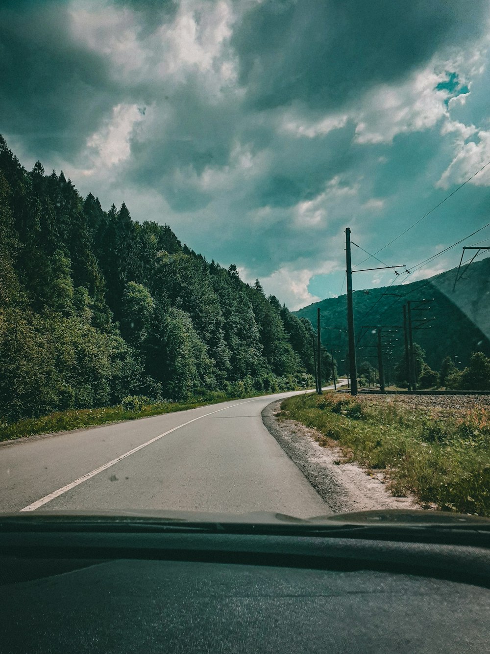 gray concrete road between green trees under white clouds and blue sky during daytime