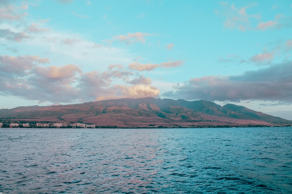 body of water near mountain under white clouds during daytime