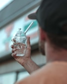 A person holds up a glass object with water inside, featuring a logo that reads 'GRAV'. The background is blurred, showing part of a sign or building.