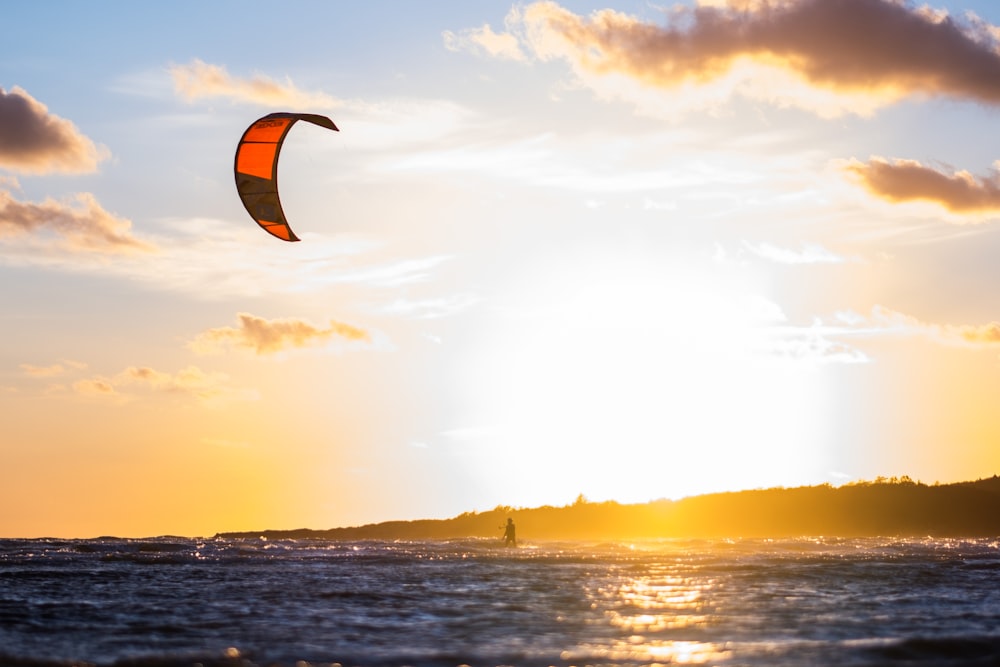 person in parachute over the sea during sunset