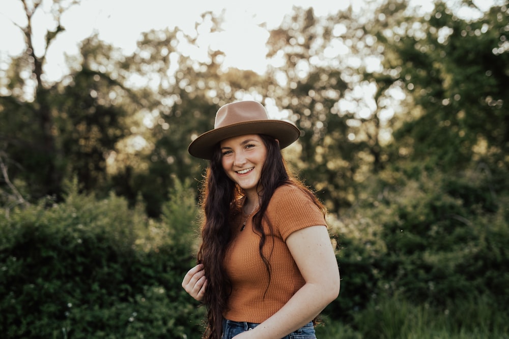 woman in blue tank top and brown hat standing near green trees during daytime