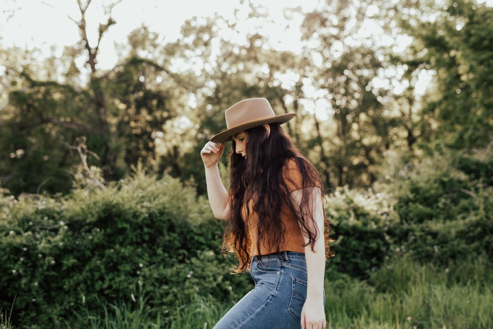 woman in blue denim jeans and brown hat standing on green grass field during daytime