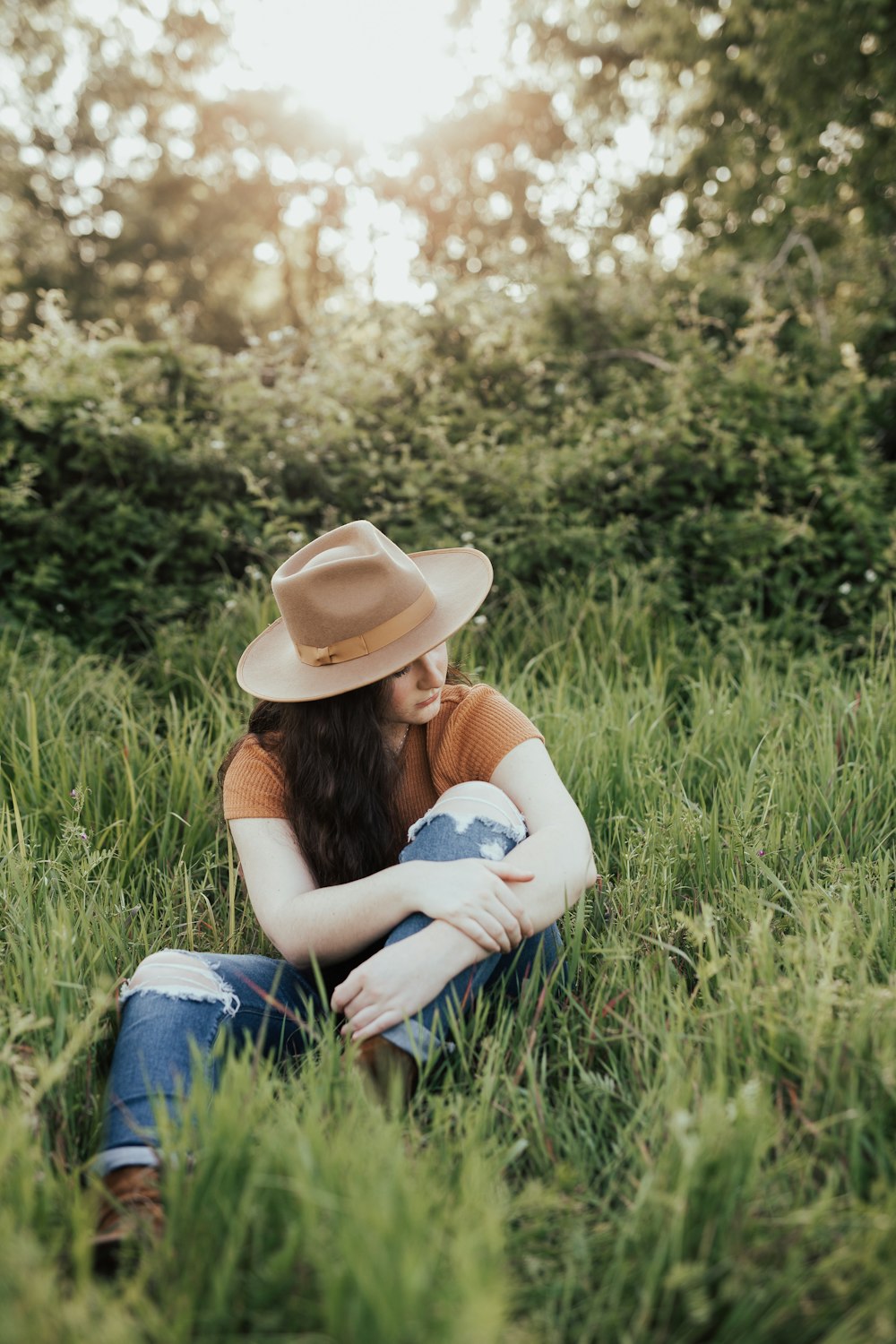 woman in white shirt and blue denim jeans wearing brown cowboy hat sitting on green grass