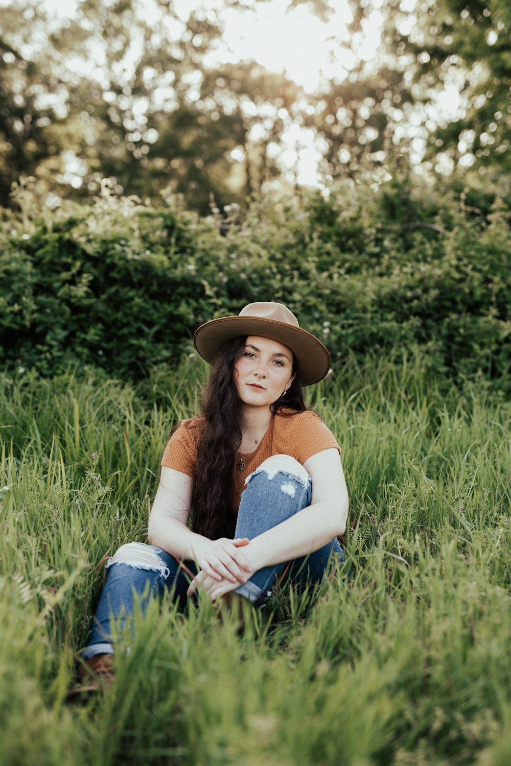woman in blue tank top and blue denim jeans sitting on green grass field during daytime