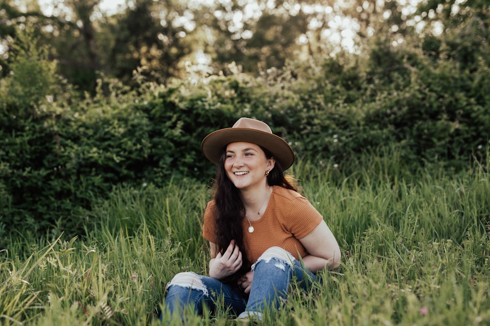 woman in blue tank top and blue denim jeans wearing brown hat sitting on green grass