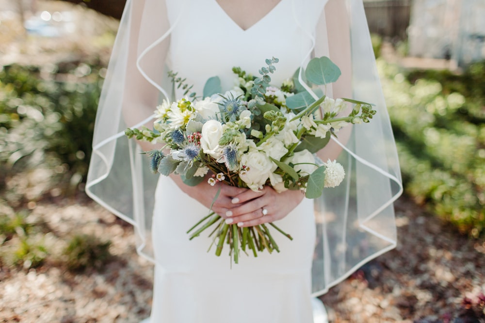 mujer en vestido de novia blanco sosteniendo ramo de flores blancas