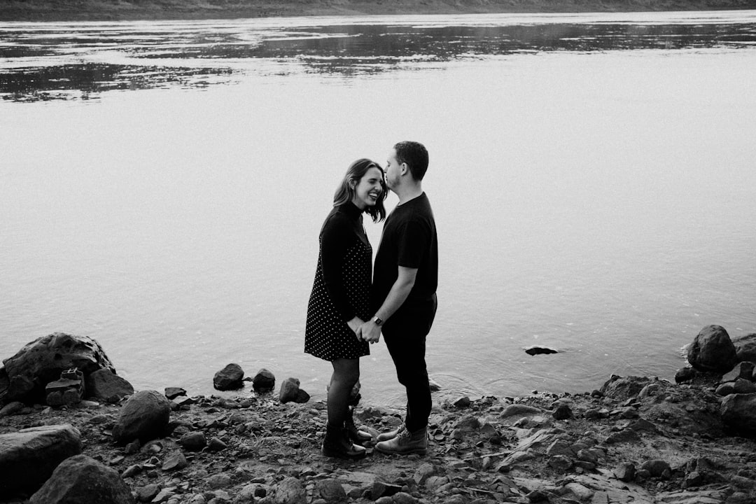 man and woman standing on rock in grayscale photography