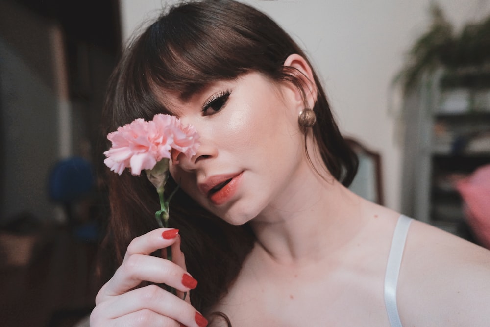 woman in white tank top holding pink flower