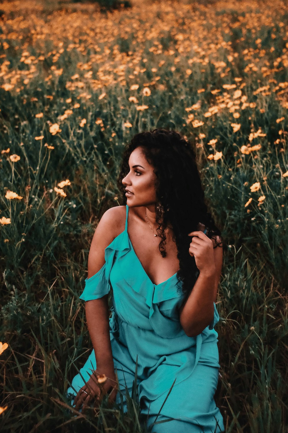 woman in teal spaghetti strap top standing on yellow flower field during daytime