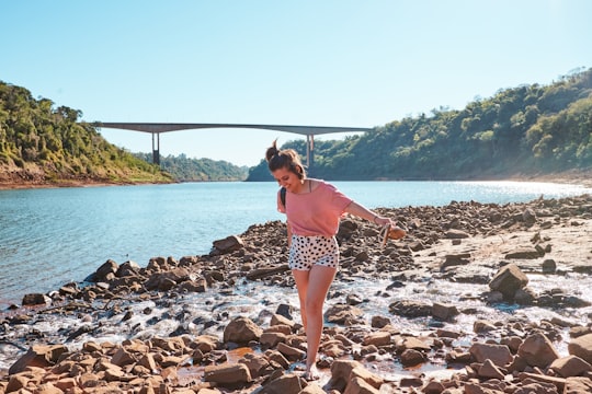 woman in red and white polka dot dress standing on rocky shore during daytime in Foz do Iguaçu Brasil