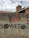 A brick wall topped with barbed wire features graffiti. The text 'I ♥ SOWETO' is painted on the wall. In the background, there are tiled roofs and an antenna.