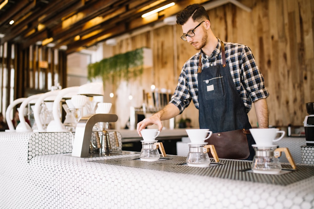 homme en chemise boutonnée à carreaux bleu et blanc debout devant la table avec des tasses