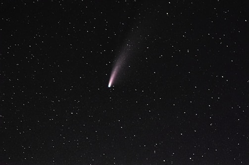 A bright comet with a faint tail is visible against a dark, starry sky. The stars are scattered evenly across the background.