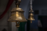 Close-up of a brass temple bell with intricate carvings, softly glowing in warm saffron light.