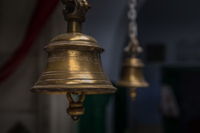 Close-up of a bell hanging in a Shiva temple, softly lit by oil lamps.