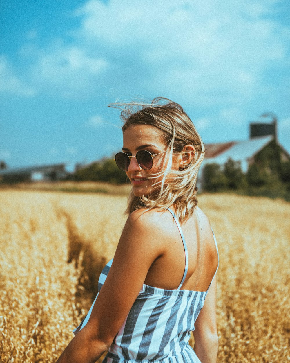 woman in white and black stripe tank top wearing sunglasses standing on brown grass field during