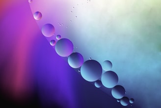 Close-up of glowing molecular spheres in purple, pink, and blue floating above sleek lab equipment on a dark purple gradient background.