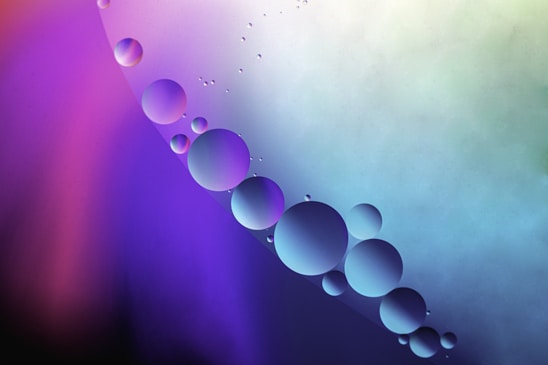 Close-up of glowing molecular spheres in purple, pink, and blue floating above sleek lab equipment on a dark purple gradient background.