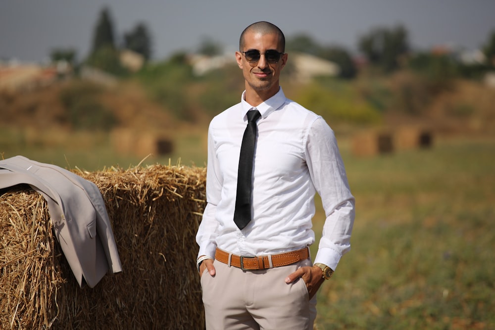 man in white dress shirt and black necktie standing on brown grass field during daytime