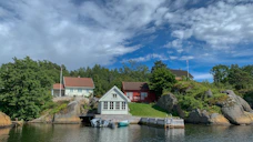 white and brown house near green trees and body of water under blue and white cloudy