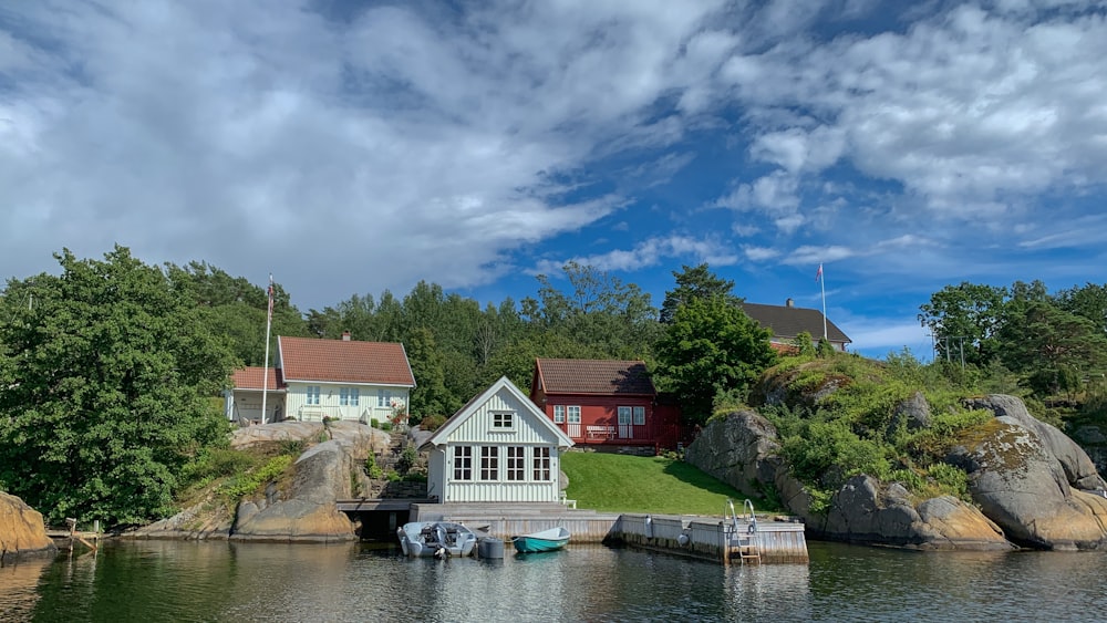 white and brown house near green trees and body of water under blue and white cloudy