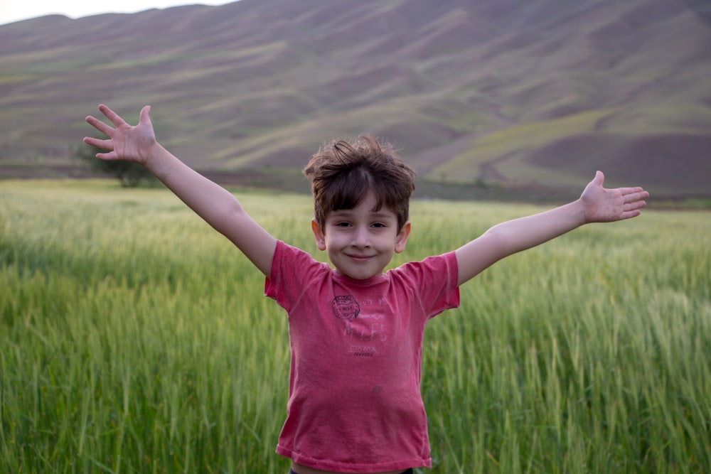 girl in pink crew neck t-shirt standing on green grass field during daytime