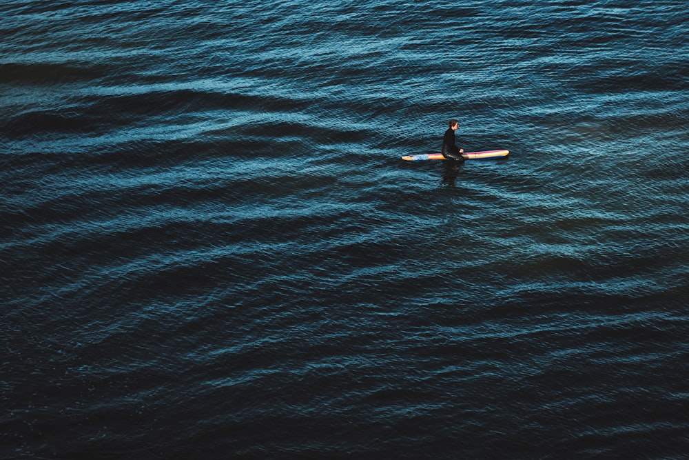 昼間、青い海でサーフィンをする黒いウェットスーツを着た人